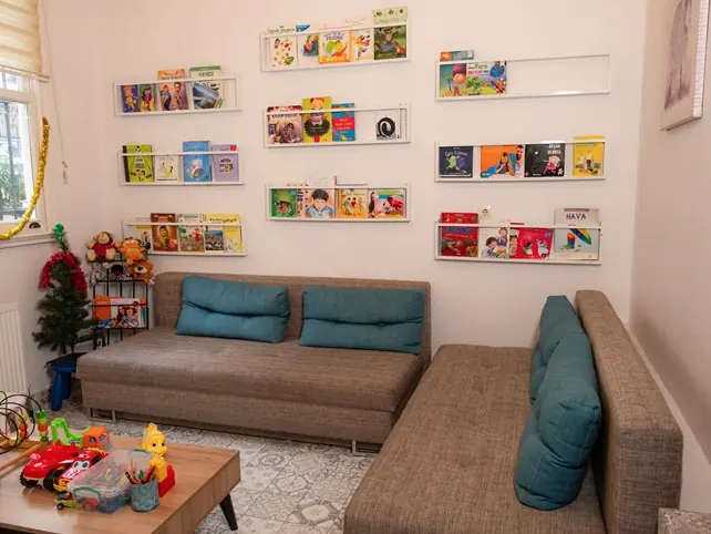 Duvar raflarında çocuk kitapları, kanepe ve oyuncaklı okuma köşesi