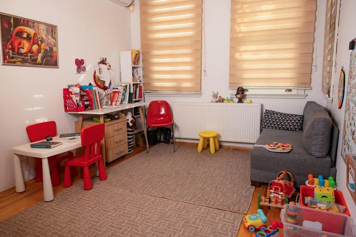 Kırmızı çocuk masası, oyuncak rafları ve kanepesi olan oyun odası